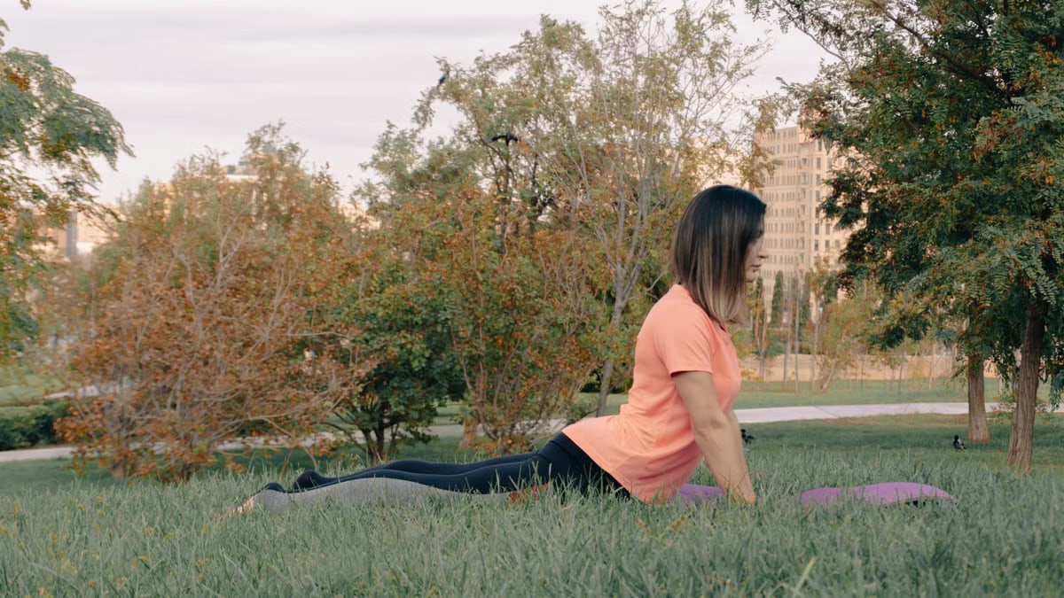 Adult woman performing yoga exercise outdoors in a peaceful park setting, surrounded by greenery.